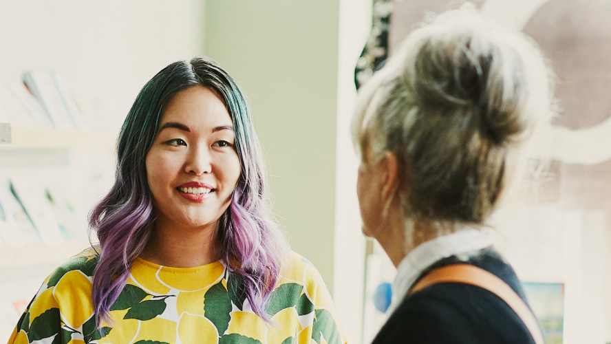 Two women engaged in conversation, one with vibrant purple hair.