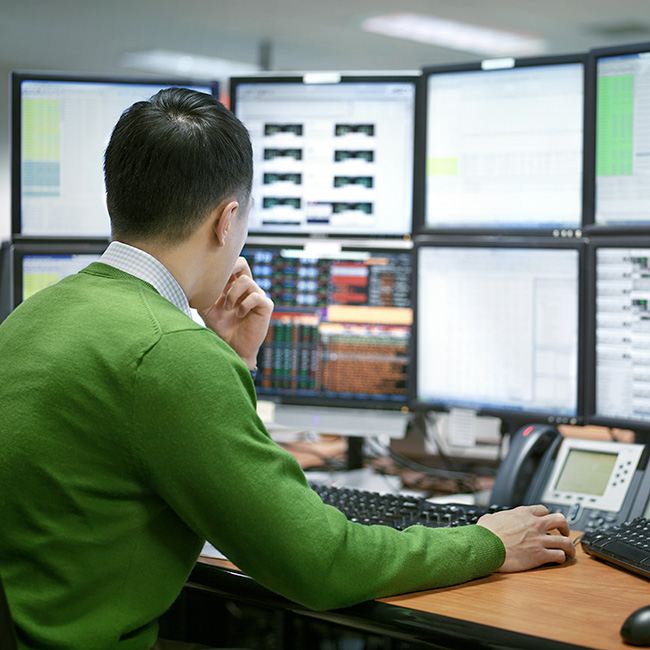 A man sitting at a desk, surrounded by computer screens displaying various data and information