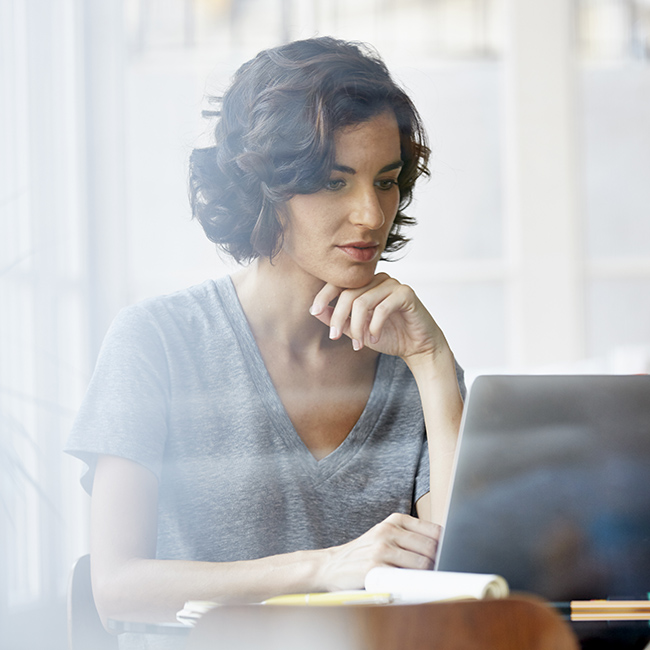 Uma mulher em um ambiente iluminado senta-se concentrada em seu laptop