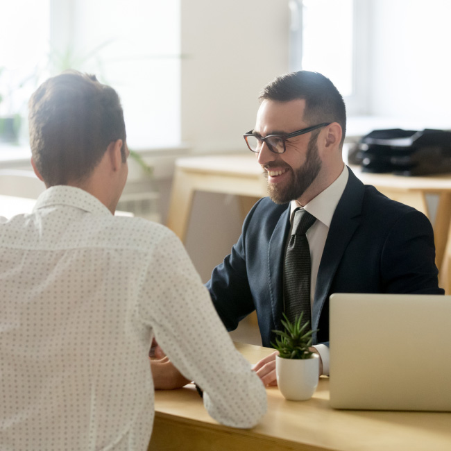 Duas pessoas vestidas com trajes formais conversam sentadas em uma mesa