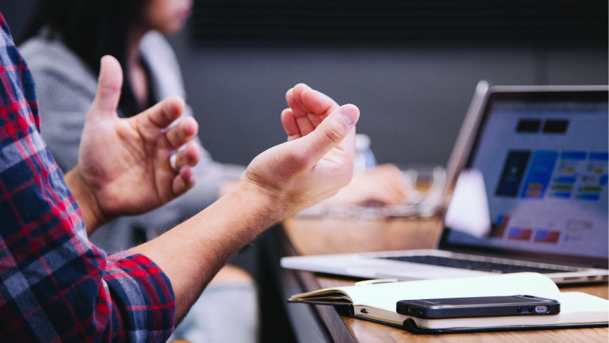 A person gesturing at a desk with a laptop, engaged in work or communication, showcasing productivity.