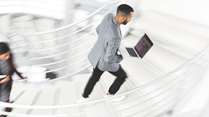 Un uomo d'affari scende con sicurezza le scale con un computer portatile in mano, incarnando professionalità e produttività.