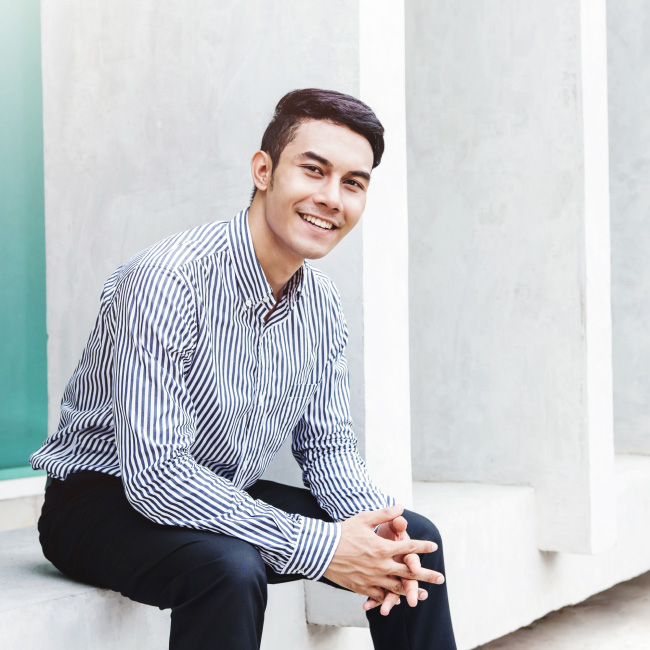 A man seated on a wall wearing a striped shirt and black pants.