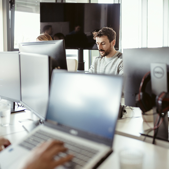 Colleagues work in a glass-walled meeting room as people walk by outside