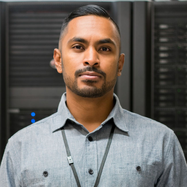 A man in a grey shirt stands in front of a server, overseeing its operations and ensuring smooth functioning.