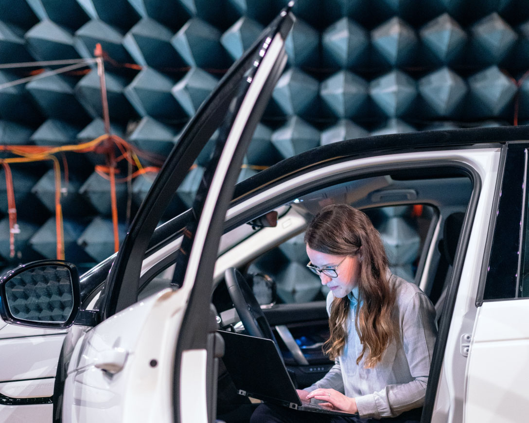 A woman in the driver's seat of a car, focused on her laptop.