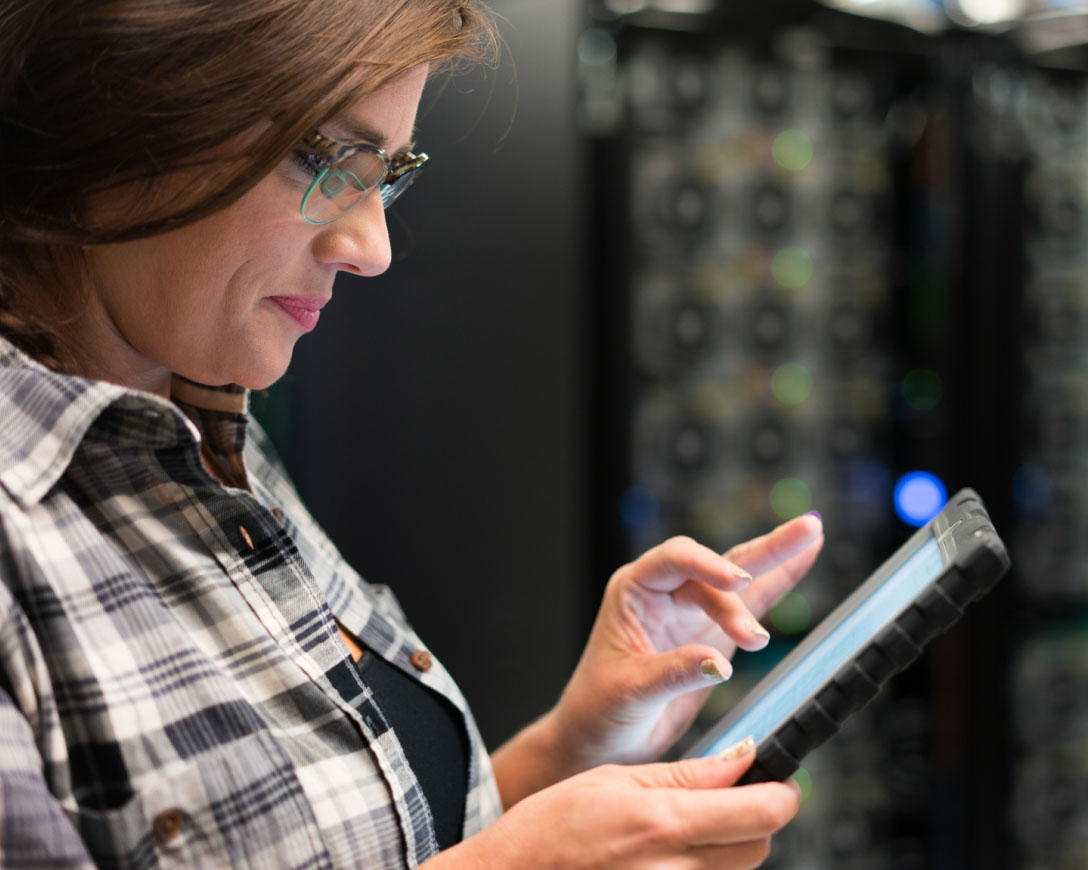 A woman in a server room, engrossed in her tablet, managing data and ensuring smooth operations.